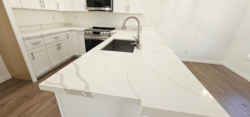 Bright modern kitchen with white cabinets, marble island, and stainless stove and sink