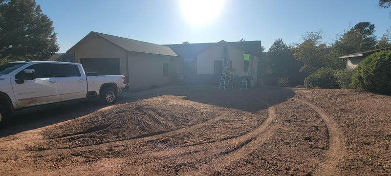 Sunlit dirt driveway with a white pickup truck beside a house and garage