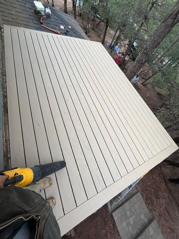 Person using a yellow power tool on a large beige roof deck outdoors.