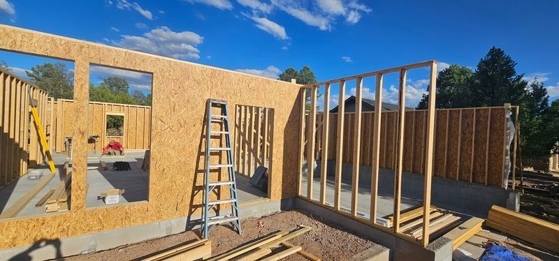 Partially framed house construction with ladders, plywood walls, and blue sky