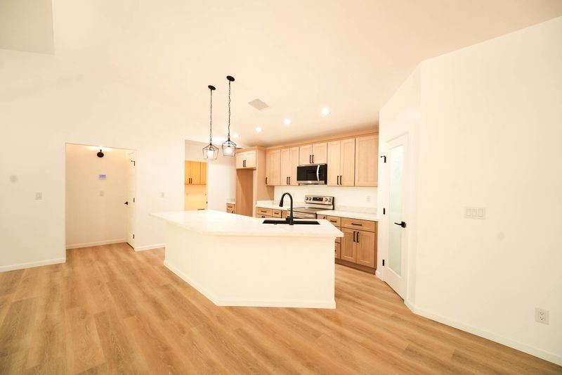 Bright open kitchen with wood floors, white island, light cabinets, and pendant lights