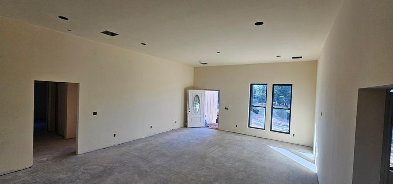 Empty unfinished room with white walls, gray floor, and windows letting in daylight