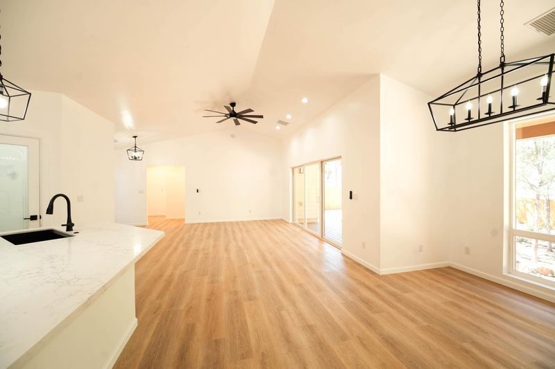 Bright, empty modern living room with wood floors, white walls, black fixtures, and large windows.