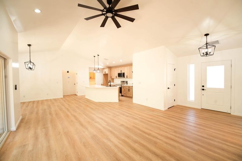 Bright open living room with wood floors, vaulted ceiling, ceiling fans, and a view into the kitchen