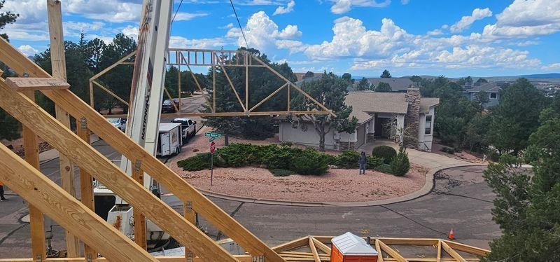 Construction site with wooden scaffolding overlooking a landscaped area and stone house under a blue sky