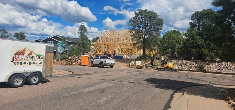 Roadside construction site with a truck, excavator, and a partially built wooden structure under a blue sky