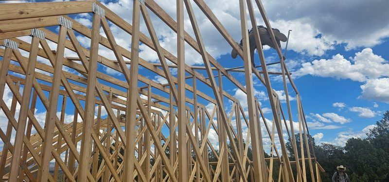 Wooden roof truss framework under construction against a blue sky with clouds