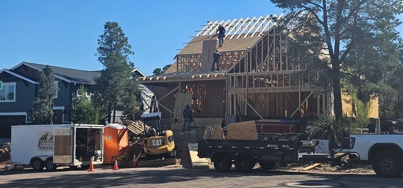 House under construction with exposed framing, workers, and construction trucks on a residential street