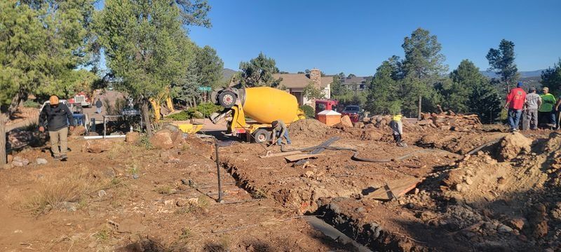 Damaged dirt road with an overturned yellow tanker and people working amid debris under a clear blue sky