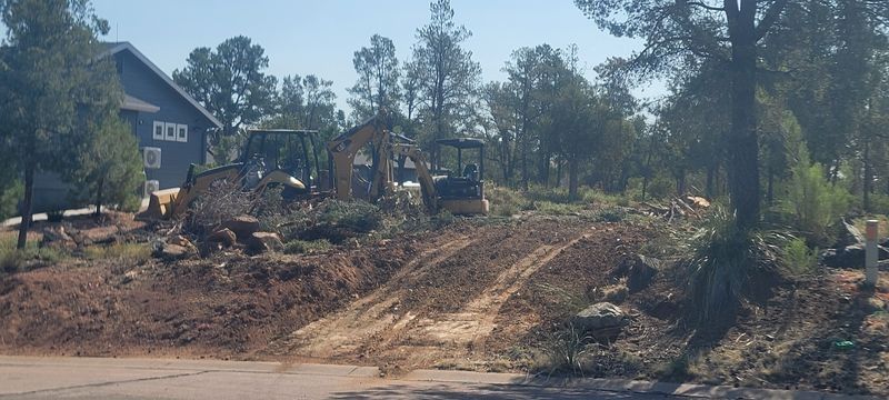 Bulldozer grading a dirt lot near houses and trees on a sunny day