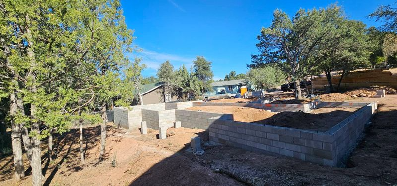 Sunlit outdoor construction site with concrete walls, dirt ground, and trees under a clear blue sky
