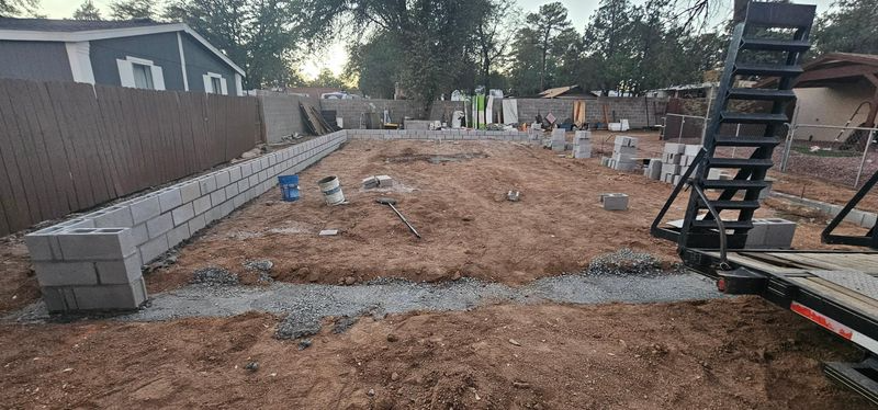 Partially excavated backyard with dirt, cinder blocks, and a metal staircase along a wooden fence