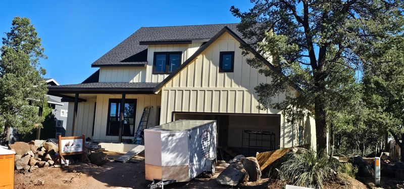 Two-story cream house with black roof, front porch, and construction debris in the yard.