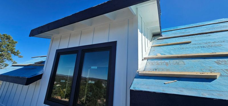 White roofline and blue shingles above a dark-framed glass door under a bright blue sky