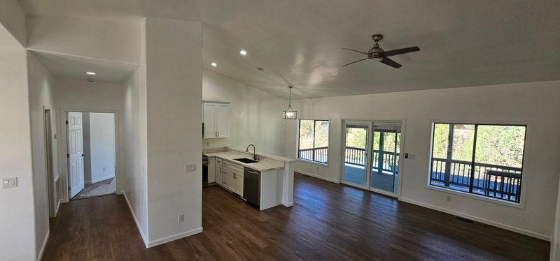 Bright empty open-plan living room and kitchen with dark wood floors, white walls, and large windows.