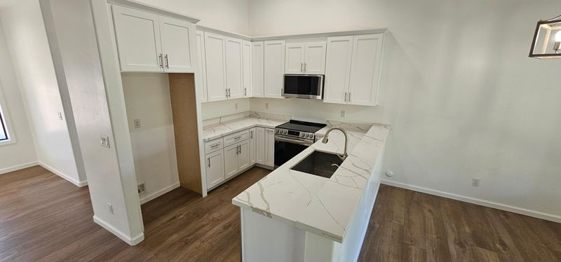 Bright white L-shaped kitchen with island, stainless appliances, wood floors, and built-in shelving