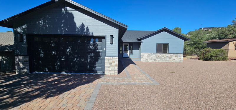 Modern house exterior with a dark garage, gray siding, and a gravel driveway under a blue sky