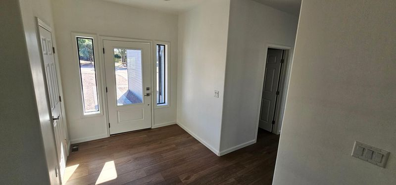Empty room with white walls, dark wood floor, and glass French doors to a bright entryway