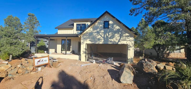 New house under construction with stone facade, garage, and dirt lot under a clear blue sky