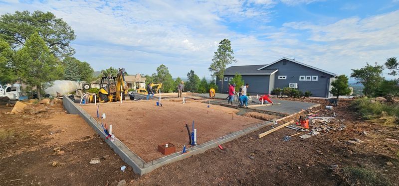 Foundation construction site with workers, concrete forms, and a dark blue building in the background