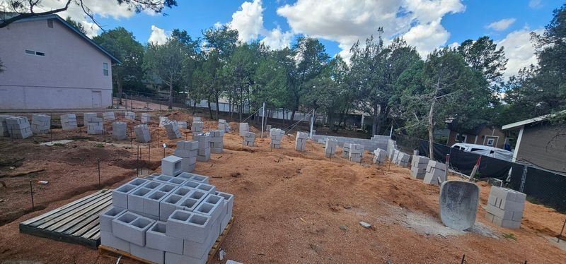 Construction site with concrete blocks, dirt foundation, and vertical rebar under a cloudy sky