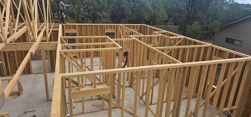Wood-framed house under construction with exposed wall studs and roof trusses on a concrete foundation