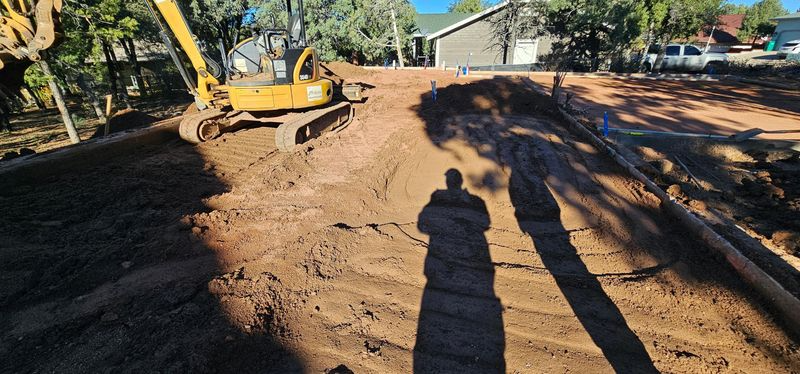 Construction site with excavator leveling a dirt driveway under bright sun