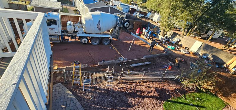 Construction workers pouring concrete in a backyard beside a house and fence