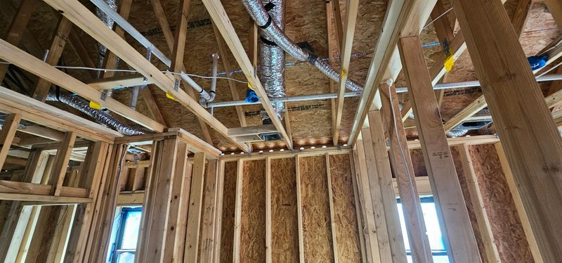 Interior of a wood-framed house under construction, with exposed studs, rafters, and roof trusses.
