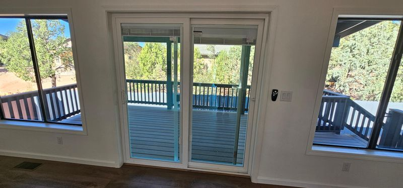 Interior view of sliding glass doors opening to a deck with black railings and trees outside