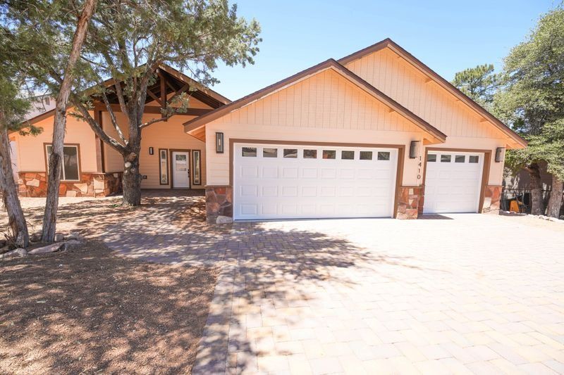 Suburban tan house with a three-car garage, trees, and a bright driveway in front