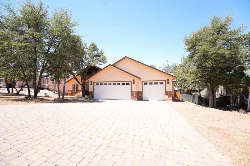 Single-story peach house with two white garage doors and a large paved driveway, surrounded by trees.
