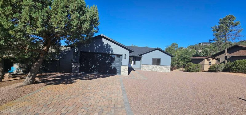 Modern gray house with a brick driveway, surrounded by trees under a clear blue sky