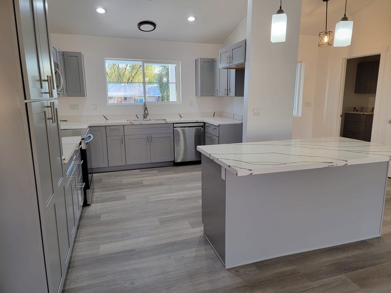 Modern kitchen with gray cabinets, white island, pendant lights, and a window over the sink.