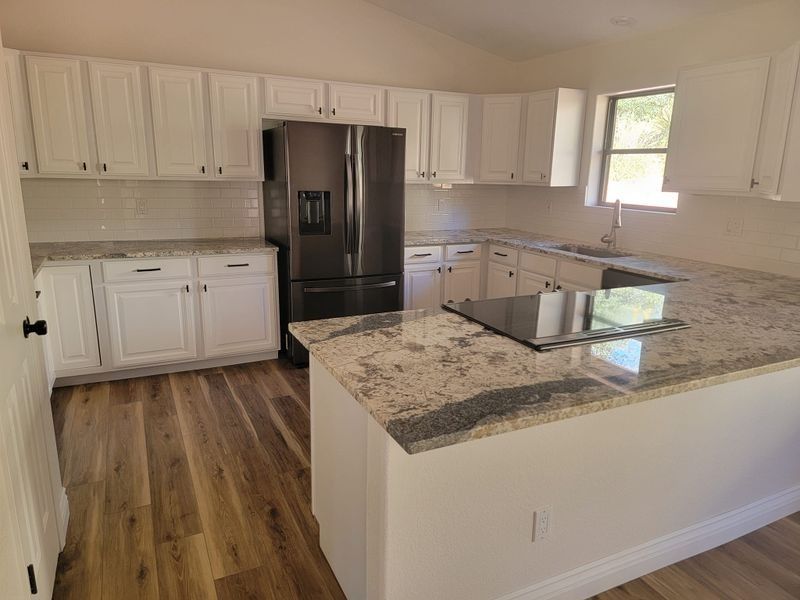 Bright modern kitchen with white cabinets, black refrigerator, and granite island countertop