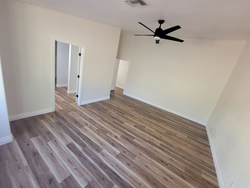 Empty unfurnished room with light wood floors, white walls, and a black ceiling fan