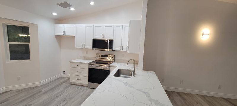 Modern white kitchen and living area with island, gray flooring, and wall sconces