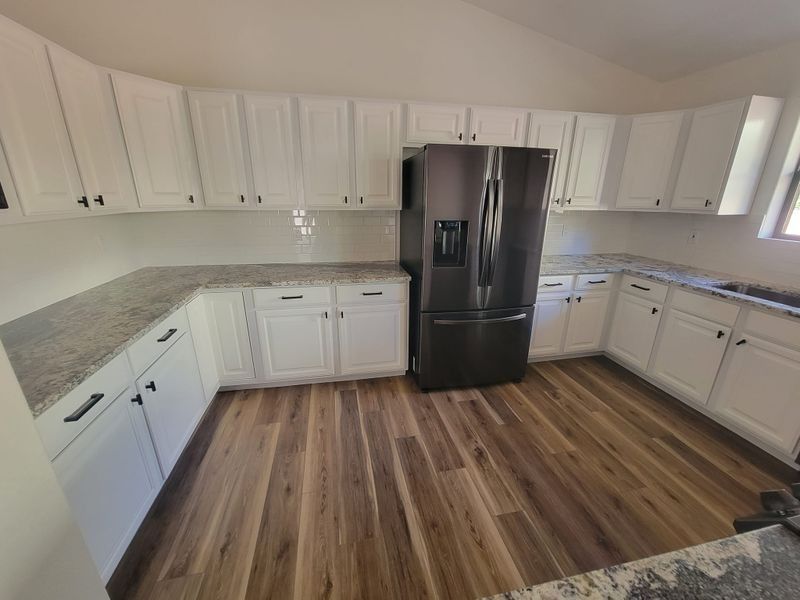 Modern kitchen with white cabinets, gray countertops, black refrigerator, and wood-look flooring