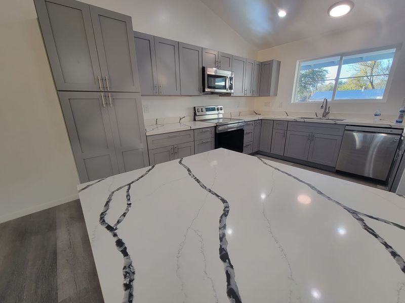 Modern gray kitchen with white marble island, stainless appliances, and large window.