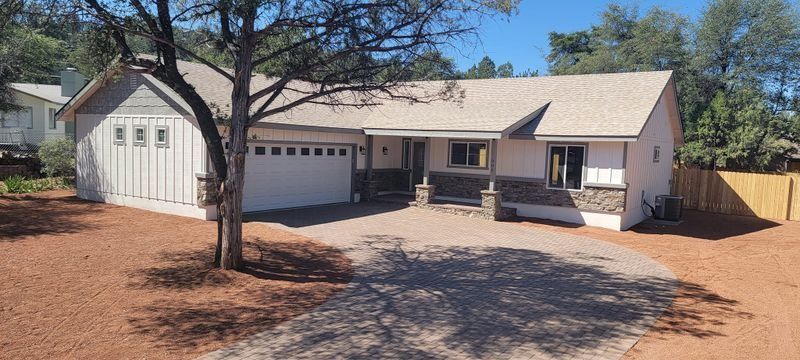 Single-story beige house with double garage, front porch, and large driveway under a clear sky