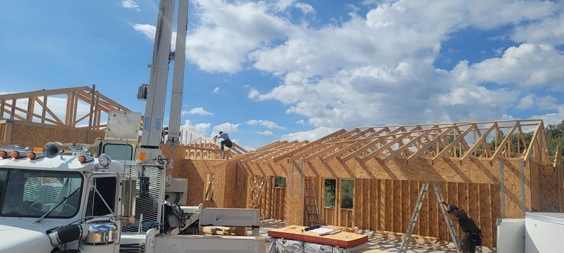 Construction site with wooden house framing, a crane, and a truck under a blue sky