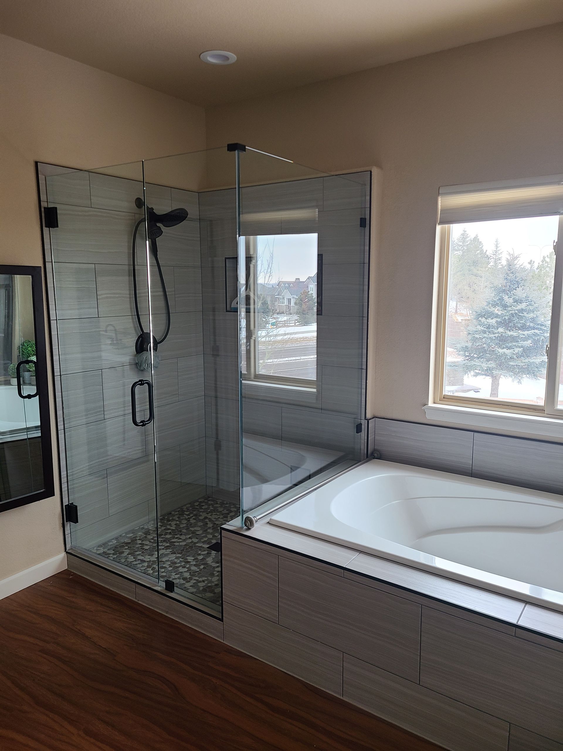 Modern bathroom with a glass shower, built-in tub, and wood-look flooring.