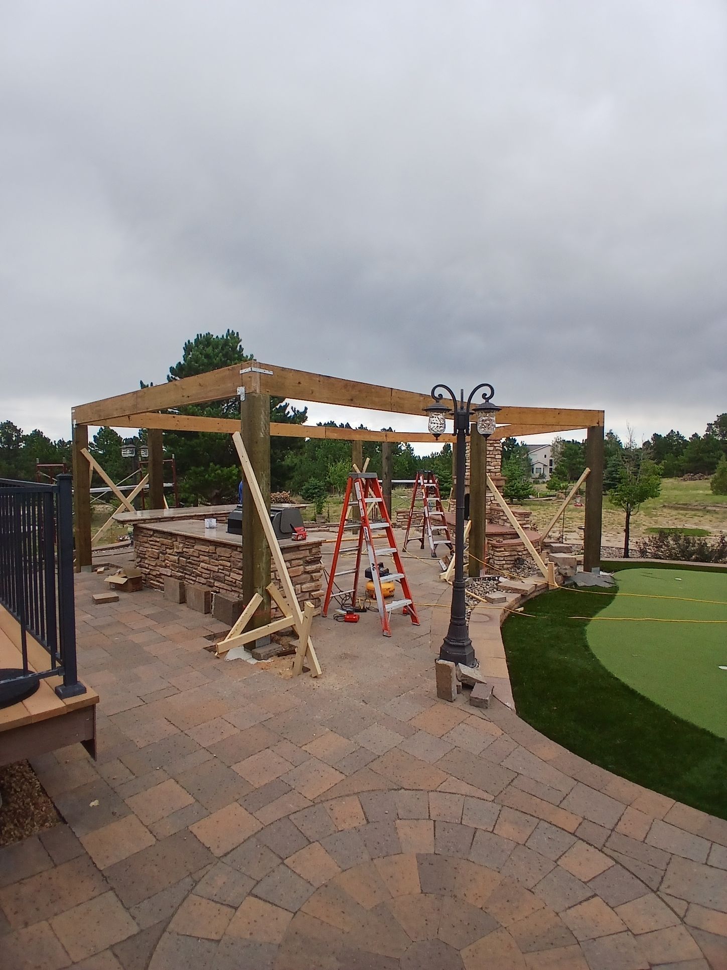 Wooden deck with a house in the background, concrete patio, and yard with dry grass under a blue sky.