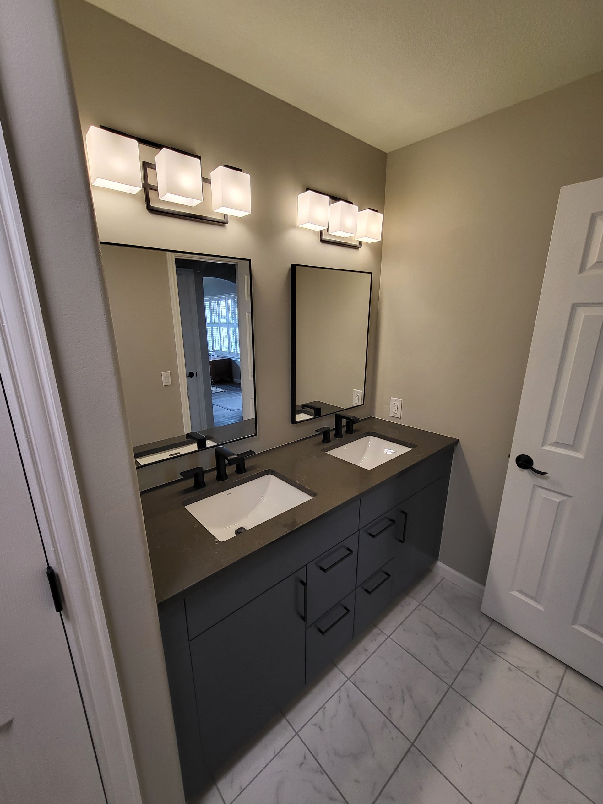 Gray bathroom with a double vanity, two mirrors, and overhead lighting.