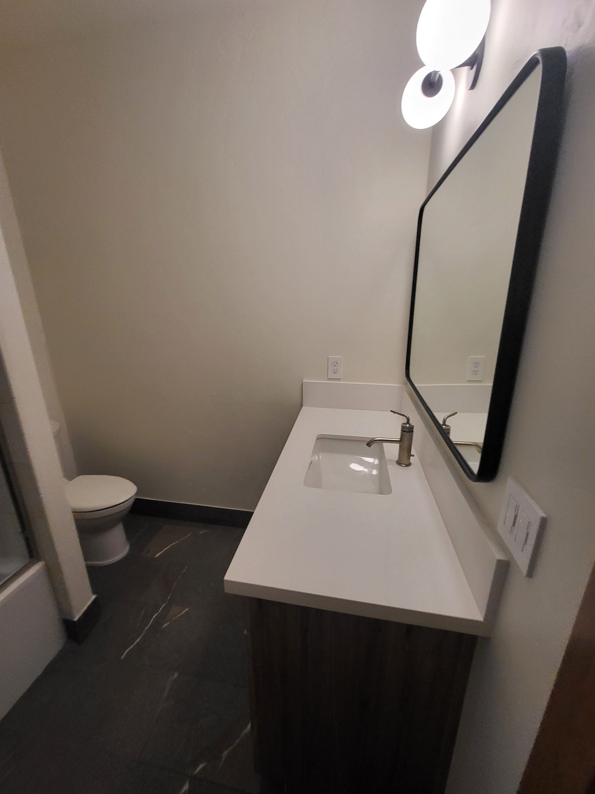 Bathroom with white countertop, black-framed mirror, dark cabinet, and toilet on the left.