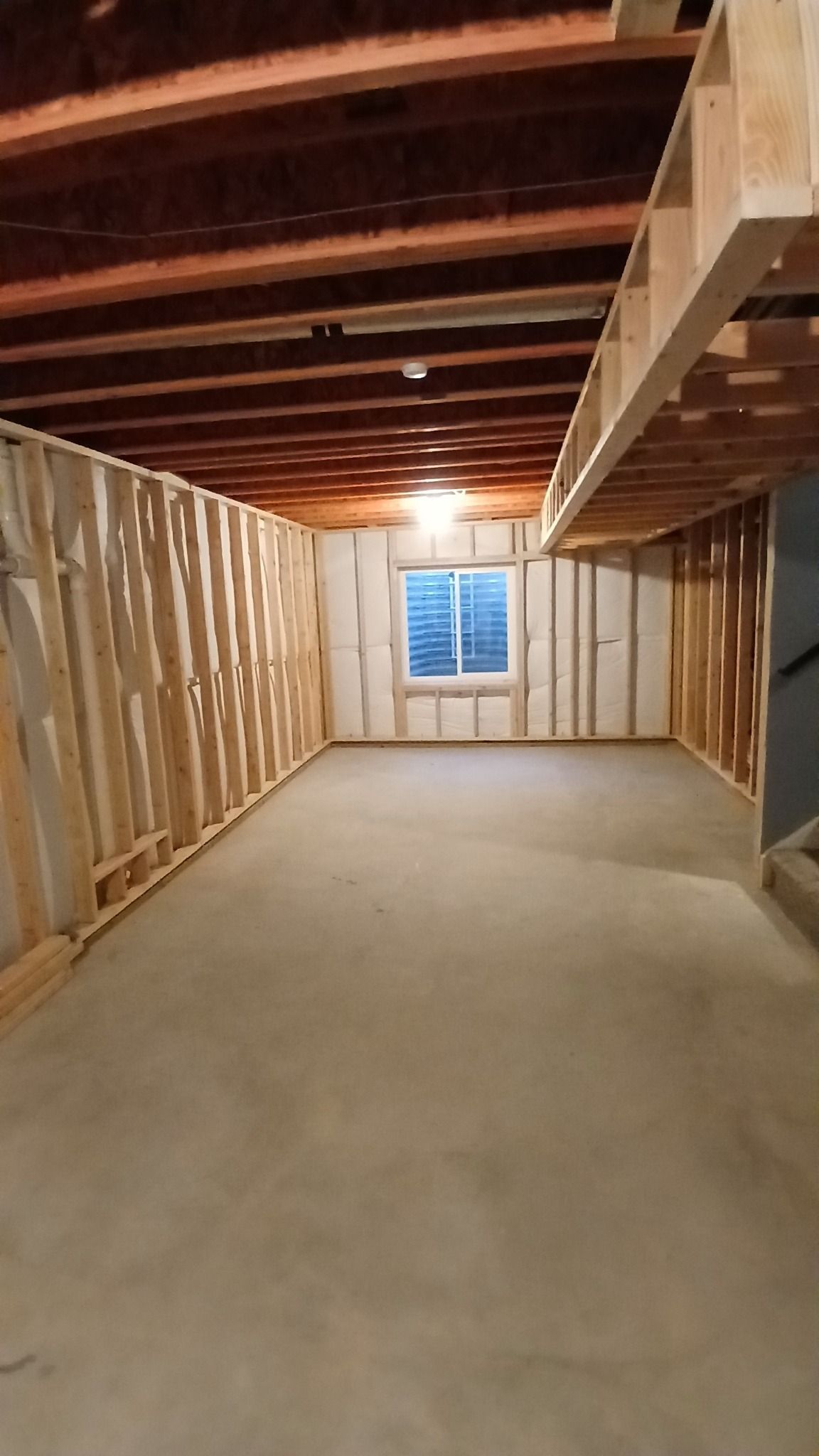 Unfinished basement with concrete floor, exposed wood beams, and partially framed walls.