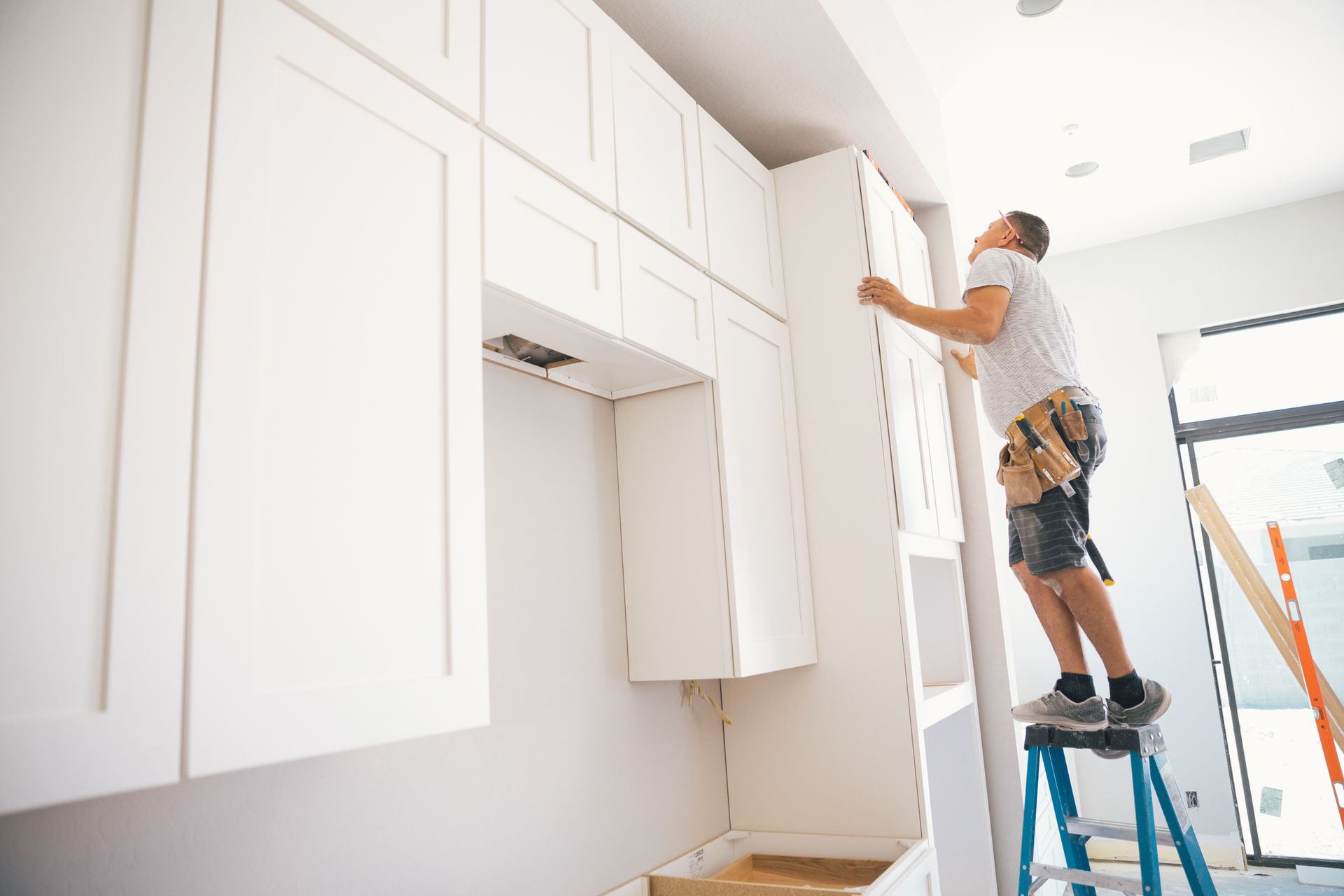 A man is standing on a ladder installing cabinets in a kitchen.