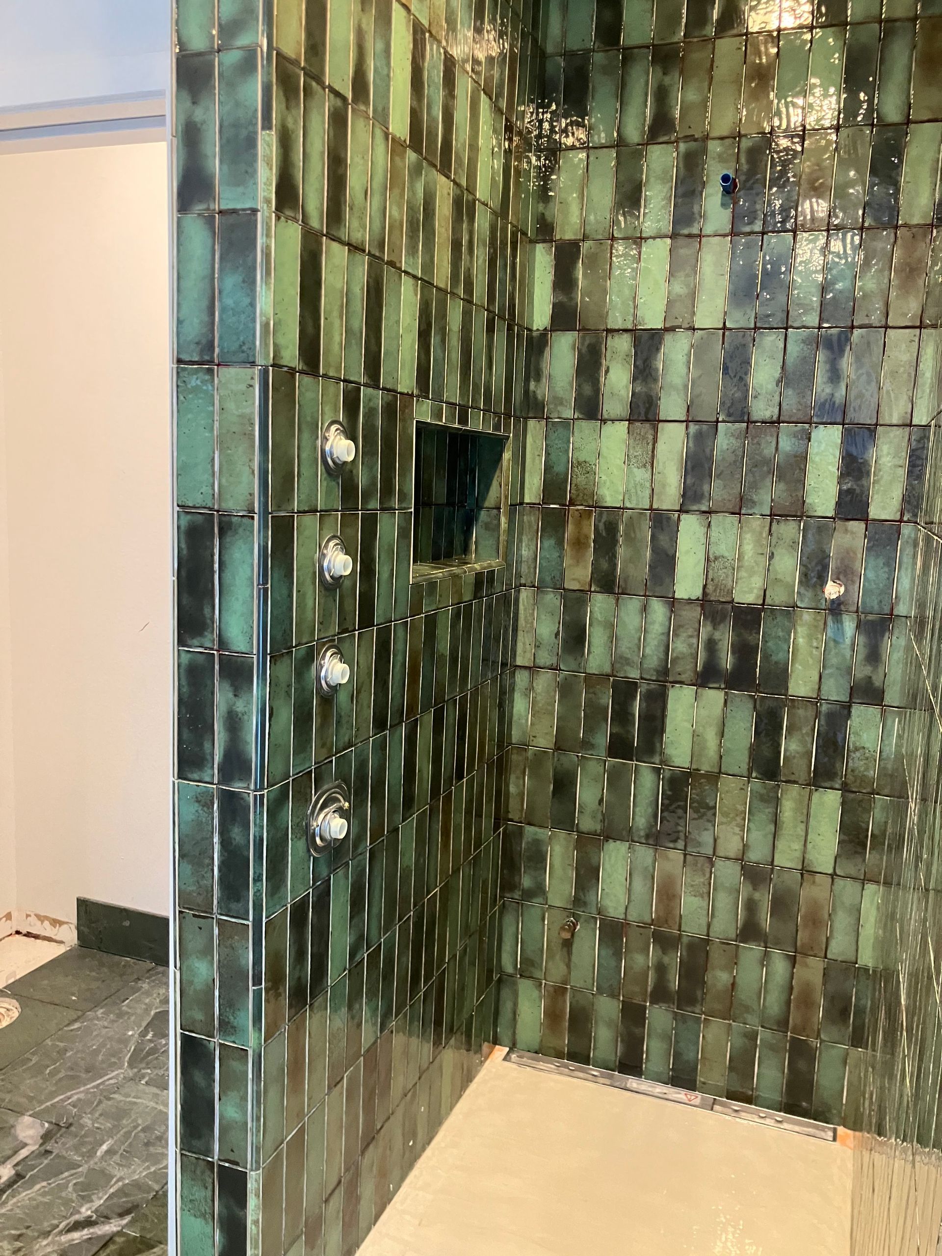 Green tiled shower with silver fixtures.