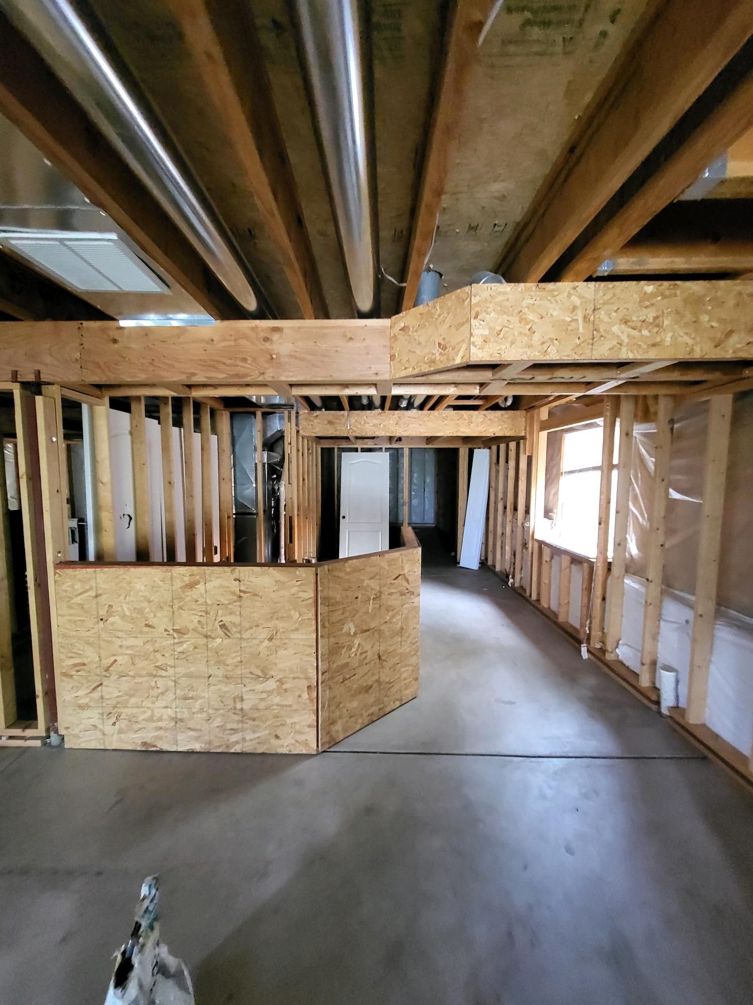 A man wearing a safety vest is repairing the ceiling of a house as part of a basement remodel.