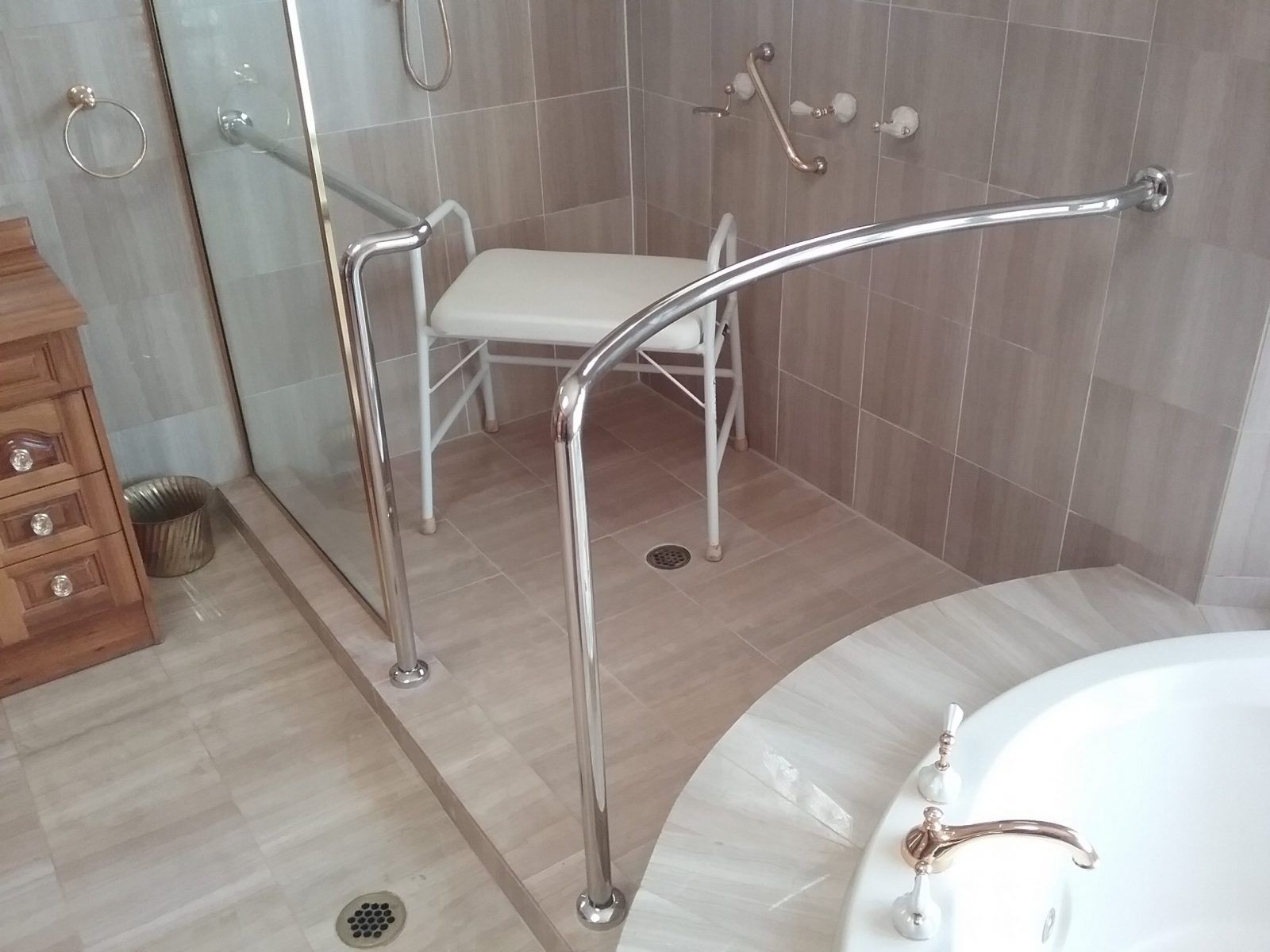 A roll-in shower with a white seat and chrome grab bars, located in a tiled bathroom next to a bathtub — Highlander Metals in Kirrawee, NSW